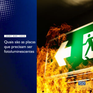 Imagem ilustrativa de placas fotoluminescentes de saída de emergência e rota de fuga, conforme a ABNT NBR 16820, aplicadas em parede de corredor industrial.
